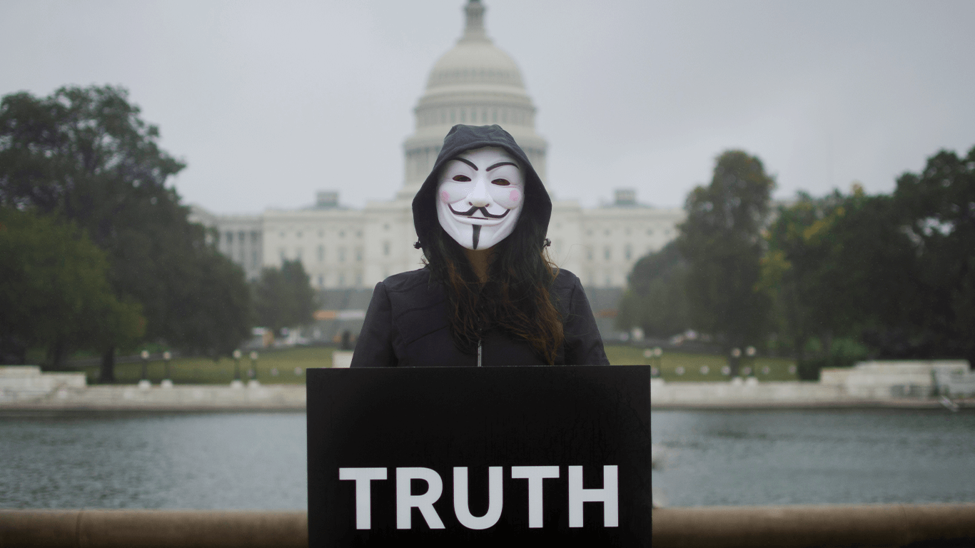 masked activist holding sign in front of white house